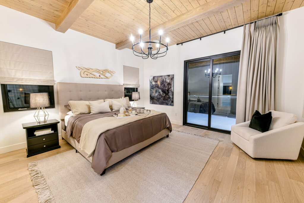 Monarch Homes, primary bedroom showcase featuring wooden flooring, beige accents, modern lighting, and walkout deck in Grande Prairie, Alberta, Canada.